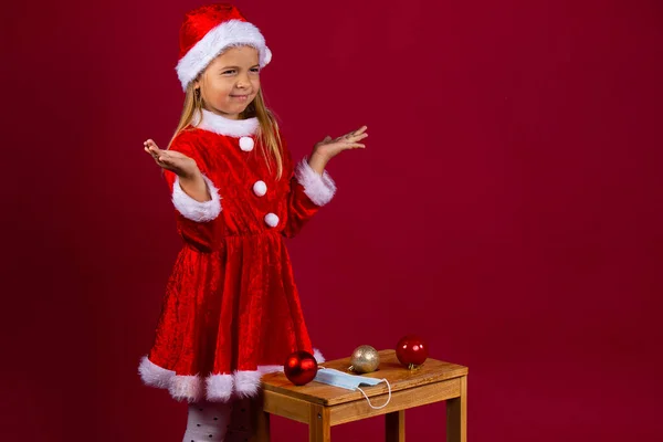 Niña Navidad costum confundido en la elección de accesorio árbol de Navidad, no entiendo el significado de la máscara, fondo rojo — Foto de Stock