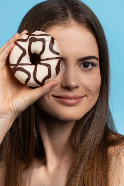 Досить біла жінка з глазурованим білим і чорним шоколадним пончиком на її очах. Ізольовані на синьому фоні . — стокове фото