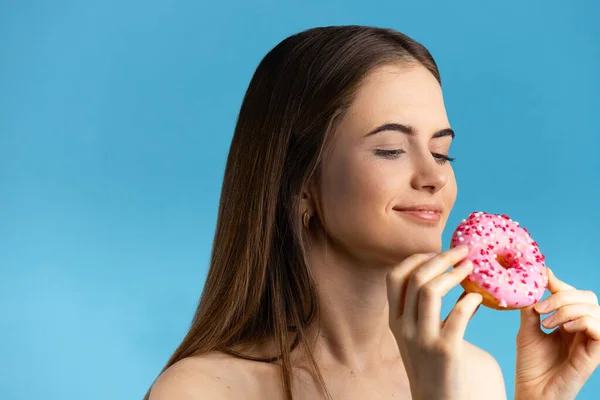 Мила дівчина хоче з'їсти рожевий глазурований пончик. Спокуса їжі. Студійний знімок. Ізольовані на синьому фоні — стокове фото