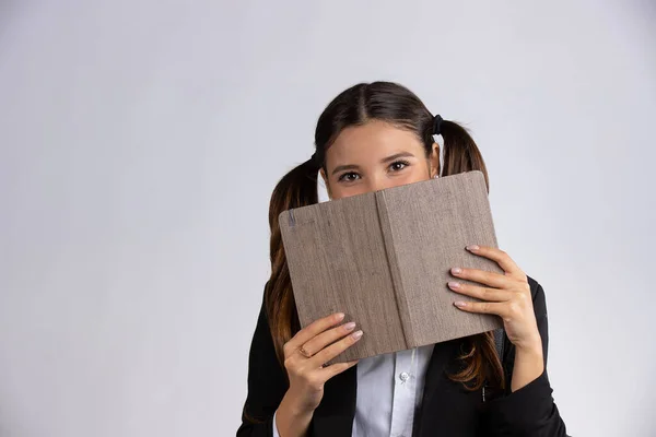 Indoor tiro de mulher alegre cobre rosto com livro didático, tem expressão alegre, isolado no fundo branco — Fotografia de Stock