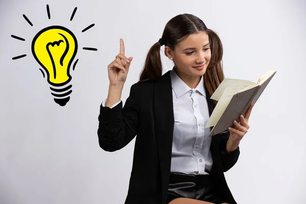 Krásná dospívající dívka čtení knihy a ukazuje prstem na žárovku, izolované na bílém — Stock fotografie
