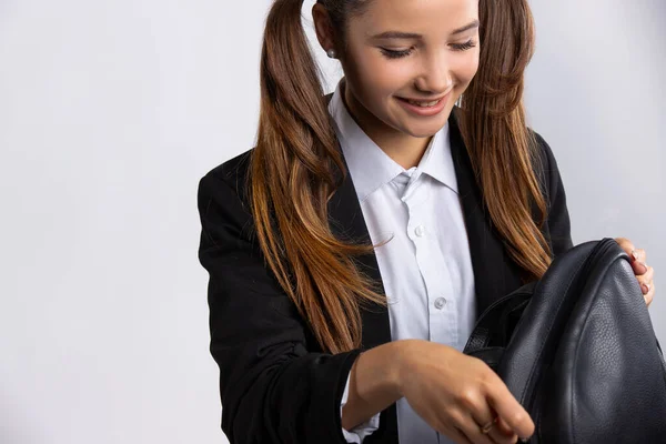 Sonriente chica caucásica con el pelo largo, buscando algo interesante. Elegante joven veinteañera chequeando su bolso negro —  Fotos de Stock