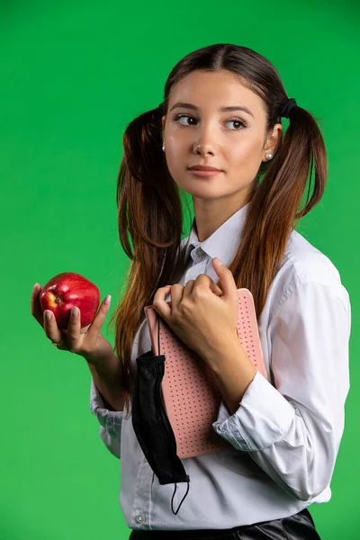 Étudiante adolescente avec pomme et masque protecteur. Adolescente étudiante tenant pomme rouge et masque de protection tout en se tenant debout sur fond vert — Photo