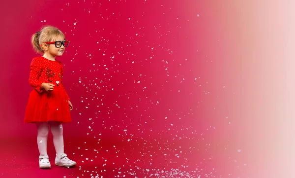 WOW... deja que nieve. Concepto de vacaciones y moda. Niña en vestido de Navidad y gafas jugando con copos de nieve. Linda belleza aislada sobre fondo rojo a blanco. Prepárate para las vacaciones de invierno. — Foto de Stock