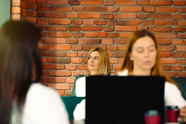 Three cute business women standing opposite each other in modern industrial brick loft style interior workplace. Focus on team leader. Waiting for an interview dreaming for successful job.