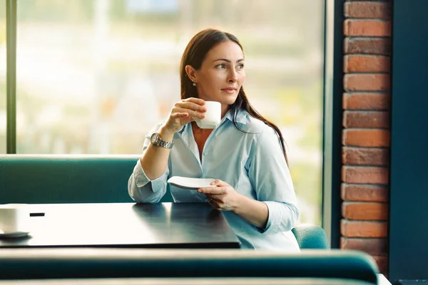Ritratto di giovane donna splendida bere il tè e guardando con sorriso fuori mentre si gode il suo tempo libero, bella donna d'affari in caffè moderno durante la sua pausa lavoro. — Foto Stock