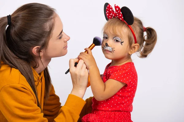 Kleines Mädchen bekommt ihr Gesicht am Karnevalsfeiertag wie eine Maus von einem Maskenbildner geschminkt. Kopierraum auf weißem Hintergrund — Stockfoto