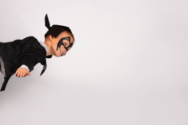 Siyah yarasa kostümlü, şapkası ve kulakları gökyüzünde şimşek gibi uçuşan mutlu süper kahraman çocuk. Beyaz arkaplanda izole edilmiş bir portre.