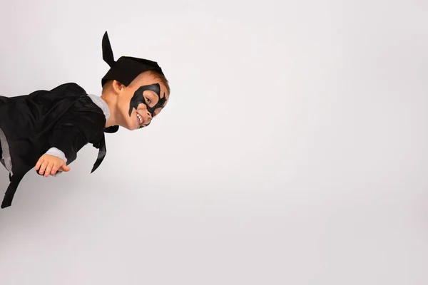 Feliz niño superhéroe en traje de murciélago negro con sombrero y orejas volando como un rayo en el cielo. Retrato aislado sobre fondo blanco con mucho espacio — Foto de Stock
