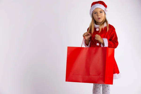 Petite fille sortie surprise par le cadeau trouvé dans le sac à provisions. Enfant en vente d'hiver avec cadeau, sur fond blanc . — Photo