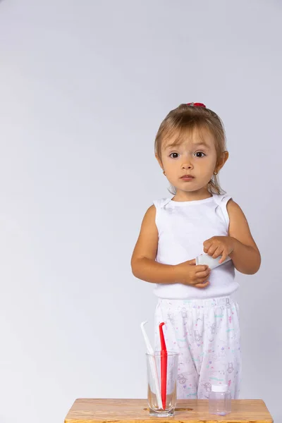 Foto interior de niña en pijama posando sobre fondo blanco con espacio vacío lateral. El niño sostiene una pasta de dientes en las manos, estando listo para cepillarse los dientes de leche, higiene diaria. — Foto de Stock