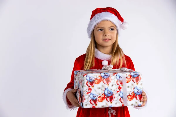 Guapo sonriente chica caucásica en Santa sombrero rojo y vestido sosteniendo regalo de Navidad en sus manos, mirando hacia fuera. Aislado sobre fondo blanco con espacio vacío. — Foto de Stock