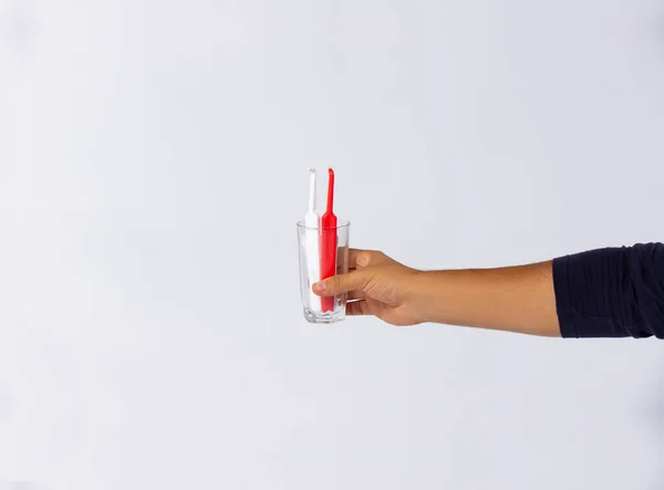 Foto de un conjunto con cepillos de dientes rojos y blancos en un vaso sostenido en mano humana sobre fondo blanco con mucho espacio, concepto dental. —  Fotos de Stock