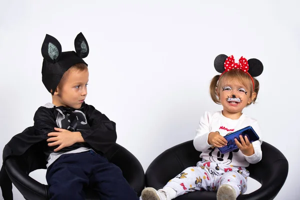 Los niños esperan Halloween con disfraces festivos. El chico se ofende, la chica no comparte el teléfono. Foto interior sobre fondo blanco. — Foto de Stock