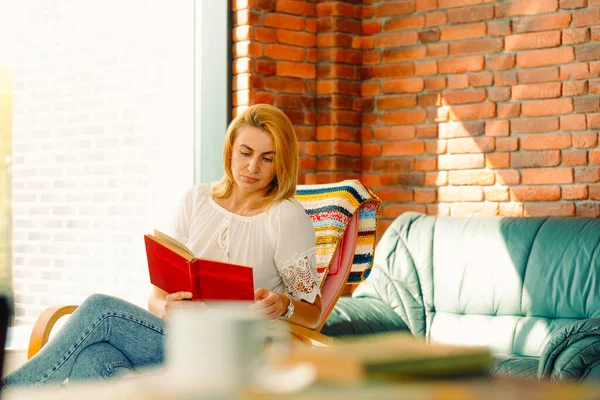 Genç ve çekici bir kadın kitap okuyor, sallanan rahat bir sandalyede oturuyor. İyi bir eğlence moralini düzeltir.. — Stok fotoğraf