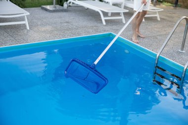 Bir insan, açık mavi bir yüzme havuzunun yüzeyinde kaymak için ağ kullanarak zahmetsizce süzülür.