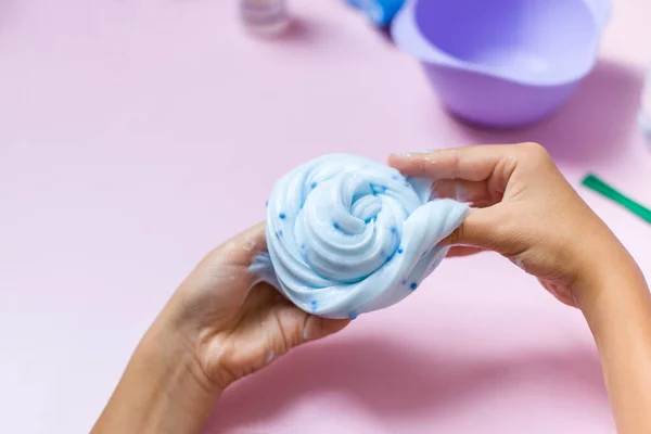 Çocuk küçük mavi topları olan mavi bir sümüklü oyuncakla oynuyor. Pembe arka planda mavi topları olan mavi balçık oyuncağı.. 
