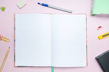 Pembe arka planda kırtasiye malzemesi olan defteri aç. Yukarıdan görüntüle.