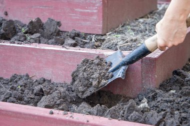Bahçede kürekle toprak kazan bir kadın, seçici bir odak noktası.
