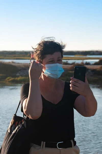 Üst düzey bir kadın, anti virüs maskesi takmış, tatildeyken selfie çekiyor..