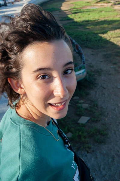 Rüzgar saçlarını savururken mutlu yüzlü kız kameraya bakar. Neşeli yüz ifadesi olan kız, rüzgar saçlarını savururken kameraya bakar. Yeşil bir kazak giyiyor..