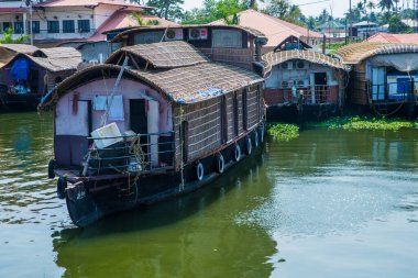 Güneşli bir günde Kerala 'nın durgun suyunun yanındaki küçük bir köyde küçük evler ve Allapuzza veya Alleppey' in pitoresk durgun sularında yüzen geleneksel yüzen yüzen yüzen yüzen tekneler görülüyor.