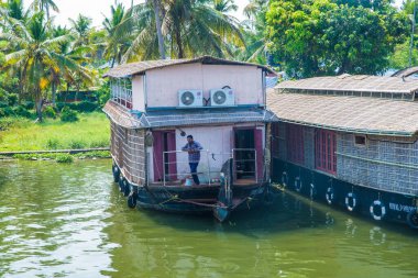 Güneşli bir günde Kerala 'nın durgun suyunun yanındaki küçük bir köyde küçük evler ve Allapuzza veya Alleppey' in pitoresk durgun sularında yüzen geleneksel yüzen yüzen yüzen yüzen tekneler görülüyor.