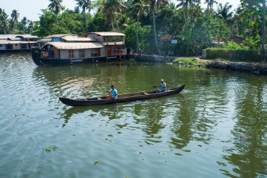 Güneşli bir günde Kerala 'nın durgun suyunun yanındaki küçük bir köyde küçük evler ve Allapuzza veya Alleppey' in pitoresk durgun sularında yüzen geleneksel yüzen yüzen yüzen yüzen tekneler görülüyor.