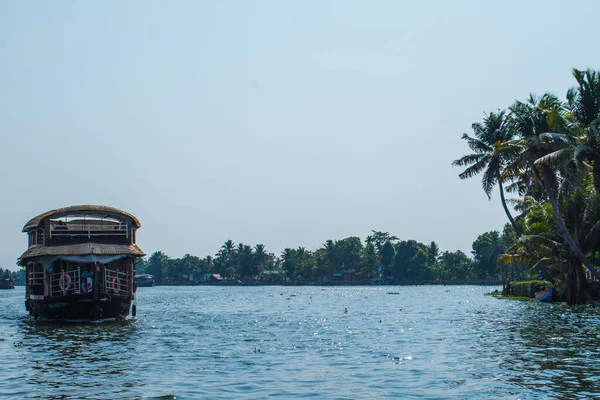 Güneşli bir günde Kerala 'nın durgun suyunun yanındaki küçük bir köyde küçük evler ve Allapuzza veya Alleppey' in pitoresk durgun sularında yüzen geleneksel yüzen yüzen yüzen yüzen tekneler görülüyor.