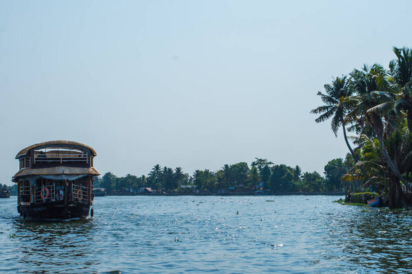 Small houses in a local village located next to Kerala's backwater on a bright sunny day and traditional Houseboat seen sailing through the picturesque backwaters of Allapuzza or Alleppey