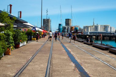 İnsanlar günlük yaşamlarını Auckland şehir merkezinde (Yeni Zelanda), bir yaz günü okyanusun yanında, ana caddelerde geçirirler. Şehir dükkanlar ve gökdelenlerle dolu. Modern bir şehir manzarası.. 