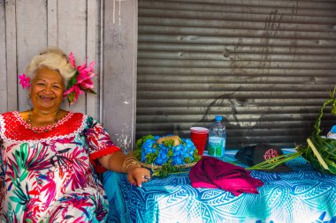 Papeete, Fransız Polinezyası 'nda gülümseyen yaşlı bir kadının portresi. Geleneksel tropik çiçekleri giydiren bir satıcı.. 