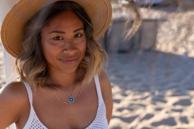 Genç ve güzel Taylandlı bir kadının, tahta bir şapka ve şık bir kolye takıp Atlantik Okyanusu 'nun kıyısındaki sahilde tek başına dinlenirken çekilmiş portresi. Kadınların özgürlük yaşam tarzı konsepti. Lizbon, Portekiz