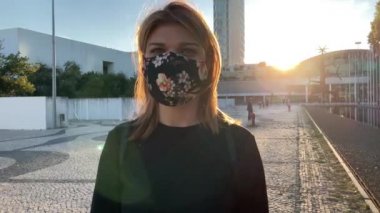 Lizbon 'daki (Portekiz) Covid-19 salgınına karşı maske takan güzel bir kadının 4k yavaş çekim görüntüleri. Arkasında bayrak direğiyle dışarıda dolaşan neşeli bir kız görüntüsü.