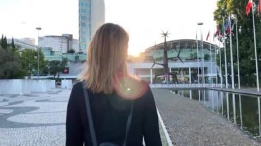 Lizbon 'daki (Portekiz) Covid-19 salgınına karşı maske takan güzel bir kadının 4k yavaş çekim görüntüleri. Arkasında bayrak direğiyle dışarıda dolaşan neşeli bir kız görüntüsü.