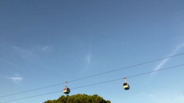 Gün batımında Lizbon 'daki Tagus nehri üzerinde uçan turistik teleferiğin 4K görüntüsü. Mavi gökyüzü arkaplanı dağınık bulutlar. Seyahat konsepti yaşam tarzı.
