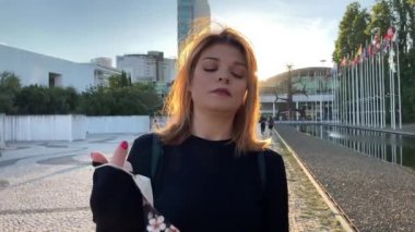 Lizbon 'daki (Portekiz) Covid-19 salgınına karşı maske takan güzel bir kadının 4k yavaş çekim görüntüleri. Arkasında bayrak direğiyle dışarıda dolaşan neşeli bir kız görüntüsü.