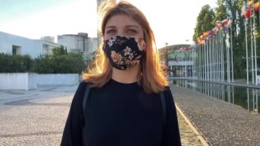 Lizbon 'daki (Portekiz) Covid-19 salgınına karşı maske takan güzel bir kadının 4k yavaş çekim görüntüleri. Arkasında bayrak direğiyle dışarıda dolaşan neşeli bir kız görüntüsü.