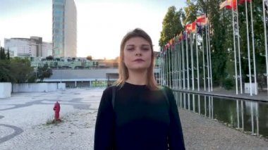 Lizbon 'daki (Portekiz) Covid-19 salgınına karşı maske takan güzel bir kadının 4k yavaş çekim görüntüleri. Arkasında bayrak direğiyle dışarıda dolaşan neşeli bir kız görüntüsü.