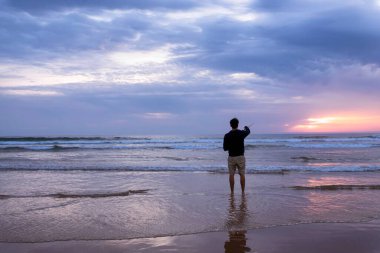 Portekiz 'in Lizbon kentindeki Costa da Caparica' da Atlantik Okyanusu kıyısında açık denizde balık tutan genç bir adam. Gün batımında sahilde oltayı tutan çekici adam. Hobi yaşam tarzı