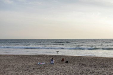 Lizbon bölgesinin en güzel sahillerinden biri olan Costa da Caparica 'da güzel bir gün batımı. Caparica 'daki Atlantik Okyanusu üzerinde açık deniz sularında sörf yapan sörfçülerle mavi saat. Lizbon, 2020