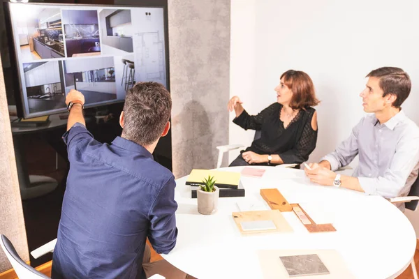 Üç genç mimar bir konferans odasında marka tanıtımı için yeni iç tasarım kavramını tartışıyor. Genç girişimciler takımda çalışıyor ve TV 'de bir projeye bakıyor.