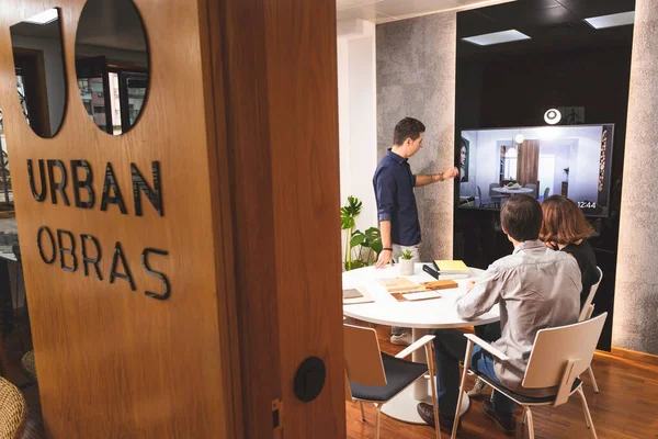 Üç genç mimar bir konferans odasında marka tanıtımı için yeni iç tasarım kavramını tartışıyor. Genç girişimciler takımda çalışıyor ve TV 'de bir projeye bakıyor.
