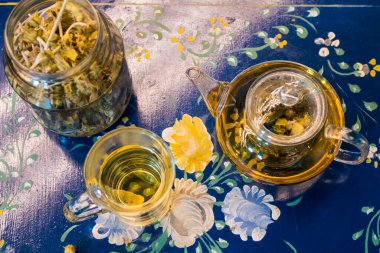 Bir fincan taze çiçek, bitki çayı ve biraz lezzetli ve sağlıklı badem kurabiyesi, vitamin açısından zengin ve az şekerli. Boşluğu kopyala. Mavi çiçekli arkaplanda üst görünüm.