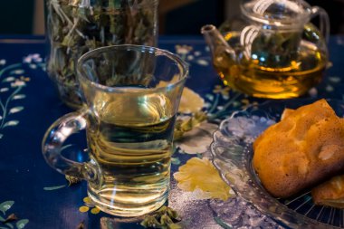 Bir fincan taze çiçek, bitki çayı ve biraz lezzetli ve sağlıklı badem kurabiyesi, vitamin açısından zengin ve az şekerli. Boşluğu kopyala. Mavi çiçekli arkaplanda üst görünüm.