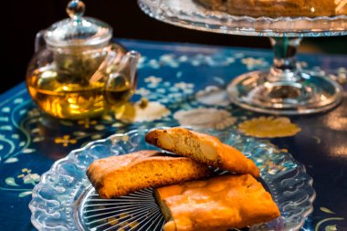 Şekerli ev yapımı tarçınlı kek, yanında bir fincan taze çiçek ve çikolatalı arap çayı ve vitamin bakımından zengin lezzetli ve sağlıklı bademli kurabiyeler. Boşluğu kopyala. Mavi çiçekli arkaplanda üst görünüm.