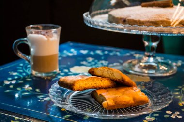 Şekerli ev yapımı tarçınlı kek, yanında bir fincan taze çikolatalı kahve ve vitamin bakımından zengin lezzetli ve sağlıklı bademli kurabiyeler. Boşluğu kopyala. Mavi çiçekli arkaplanda üst görünüm.