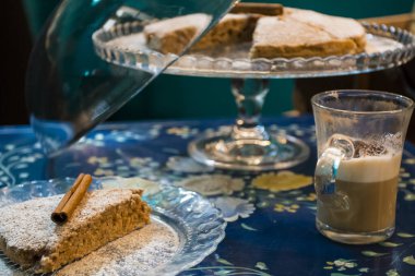 Şekerli ev yapımı tarçınlı kek, yanında bir fincan taze çikolatalı kahve ve vitamin bakımından zengin lezzetli ve sağlıklı bademli kurabiyeler. Boşluğu kopyala. Mavi çiçekli arkaplanda üst görünüm.