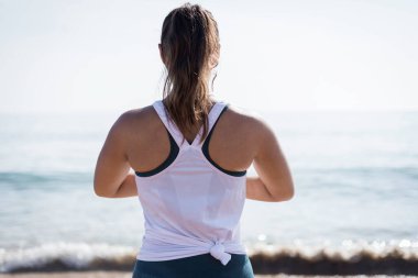 Lizbon, Portekiz 'de gün batımında plajda yoga yapan çekici genç bir kadının yakın çekimi. Egzersiz kıyafeti giymiş, güneş ışığına karşı dua eden Yoga pozu veren oyuncu bir kadın..