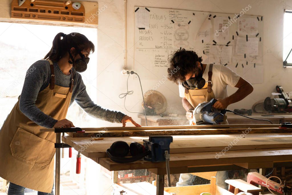Young couple of carpenter working and crafting with wood in a workshop building furniture for interior design. Young couple entrepreneurs running a small business in a carpentry. Business people.